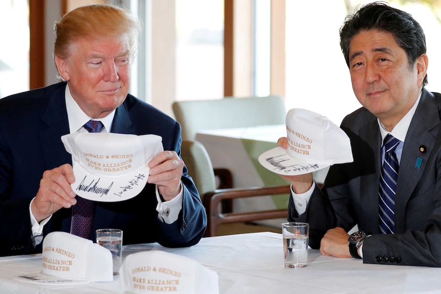 Donald Trump and Shinzo Abe hold hats they signed reading 'Donald & Shinzo Make Alliance Even Greater'.