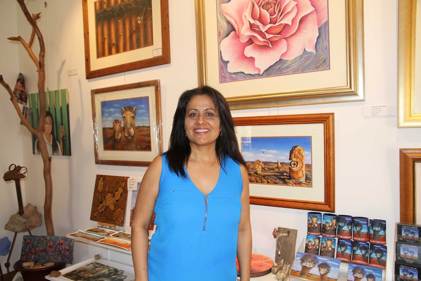 Andrea smiles at the camera. Her artwork in the background