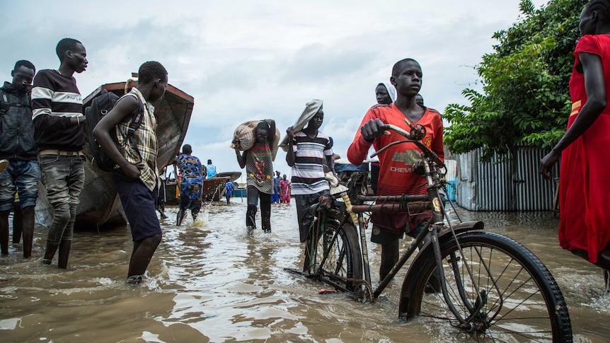 Displaced people walk with their belongings in a flooded area after heavy floods in South Sudan.