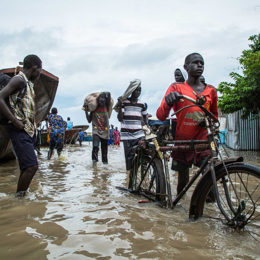 Displaced people walk with their belongings in a flooded area after heavy floods in South Sudan.