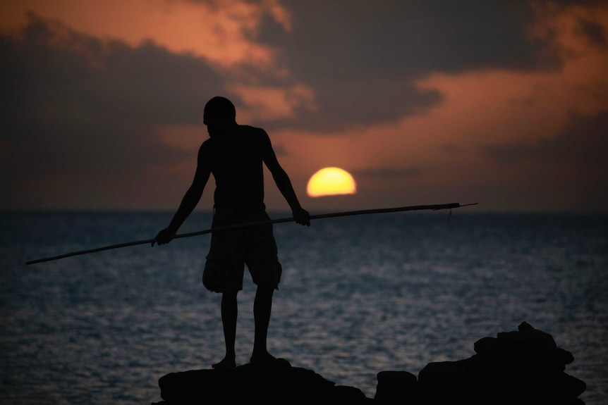 Indigenous man with spear at sunset.