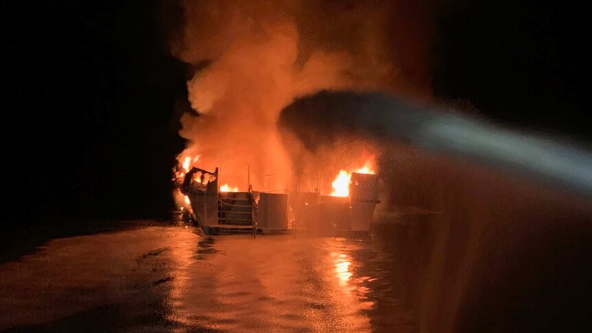 A large stream of water aimed at a fire on a boat during night time.