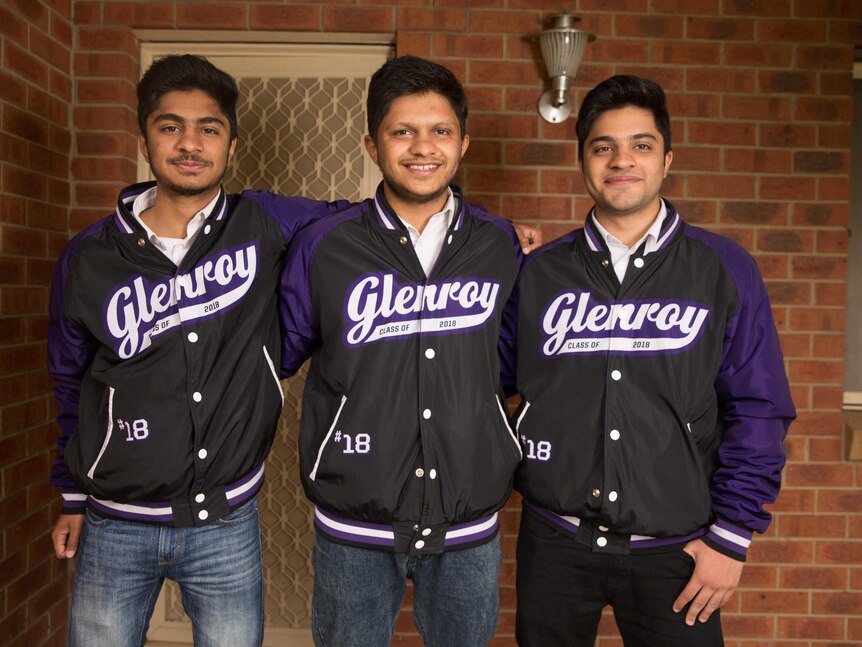 The three brothers wear purple and black Glenroy College bomber jackets and stand on their front porch together smiling