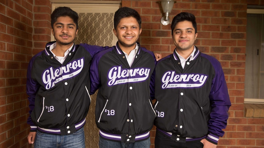 The three brothers wear purple and black Glenroy College bomber jackets and stand on their front porch together smiling