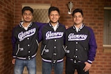 The three brothers wear purple and black Glenroy College bomber jackets and stand on their front porch together smiling