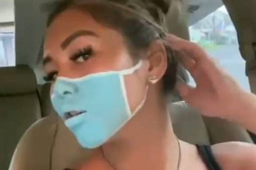A young woman posing with a fake face mask painted on her face 