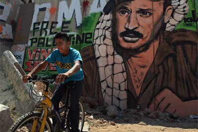 A Palestinian boy rides his bicycle beside Israel's security barrier, which has been covered with Palestinian nationalist gra...