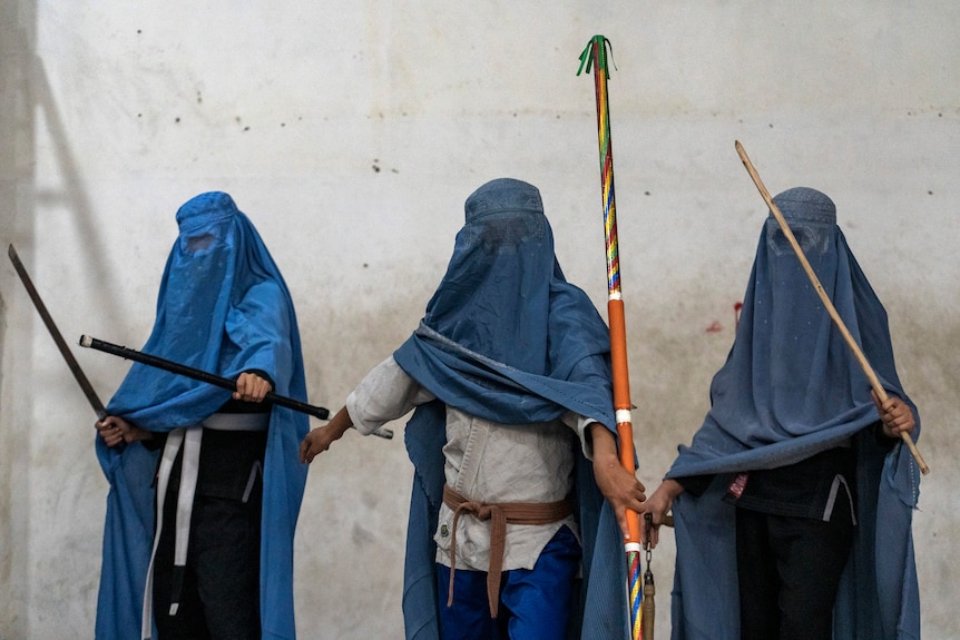 Afghan girls practicing wushu hold their equipment while wearing burkas.