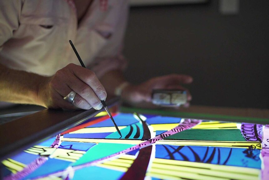 Close up of a man using a brush to paint onto a stained glass window panel