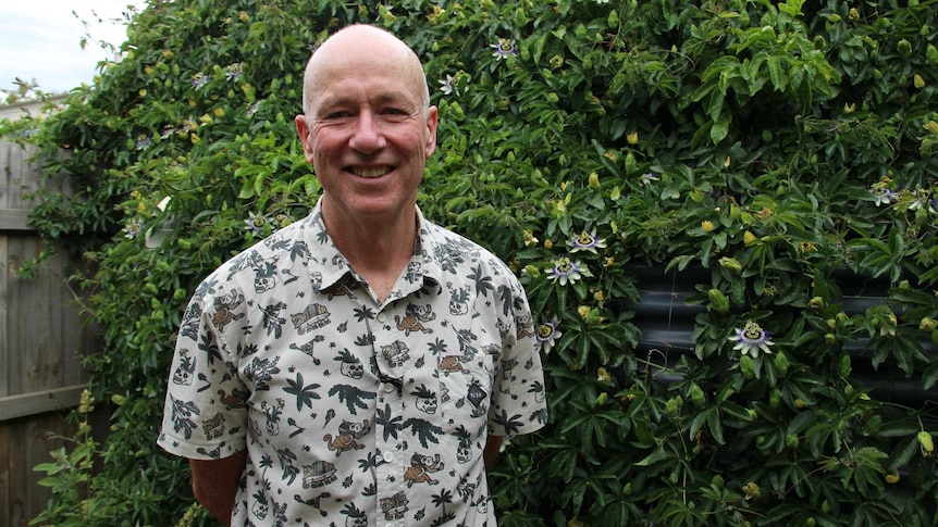 A man stands and smiles in front of a climbing plant that disguises his rainwater tank