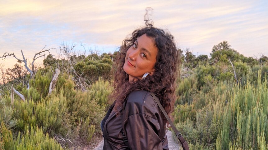 Mykaela Saunders looks back at camera from the top of headland curly hair out, wears leather jacket 