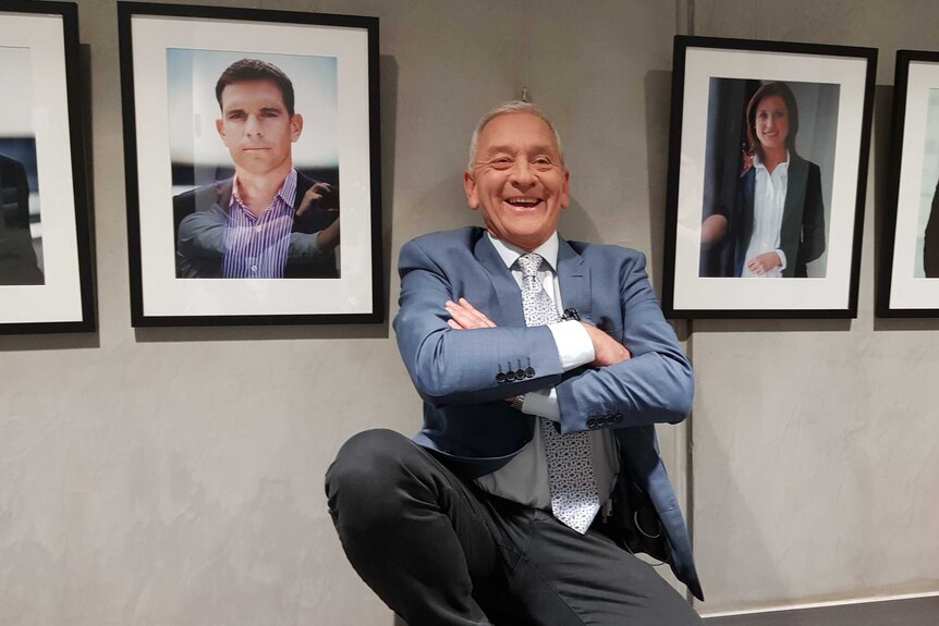 Ian Henderson is  pictured smiling in front of a wall where his publicity photo used to hang.