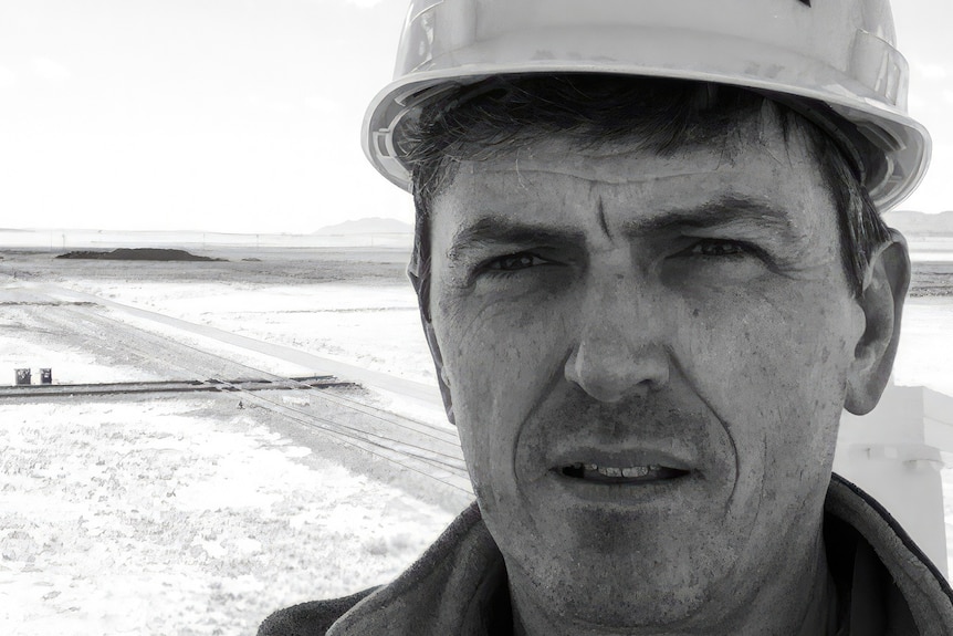 A black and white photo of Dr Chris wearing a hard hat helmet out in the field
