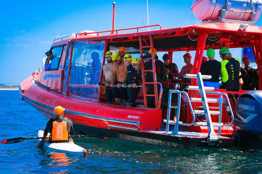 a group of people in wetsuits and swimming caps on board a boat. 