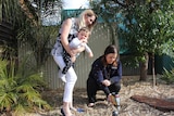 A mother smiles as she holds her baby while a health professional measures metals in the soil.