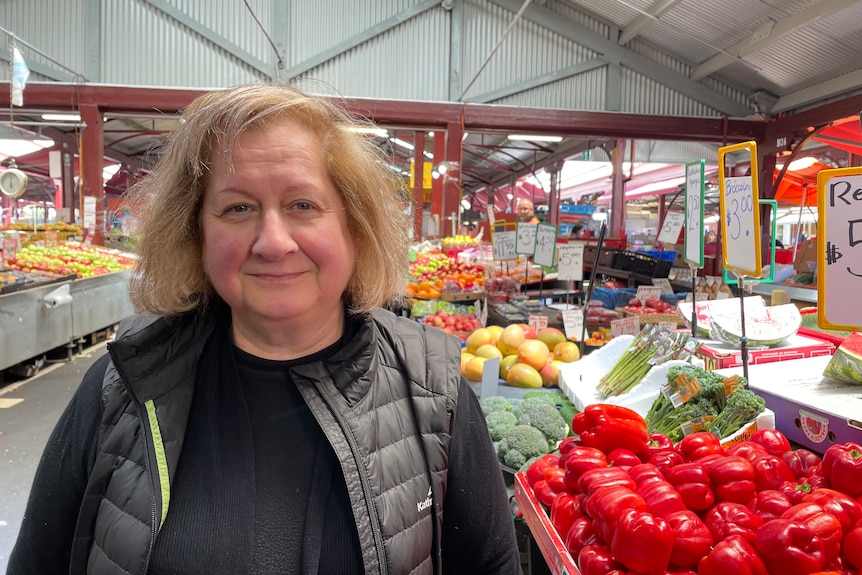 Una mujer se para frente a un puesto de frutas y verduras en un mercado.