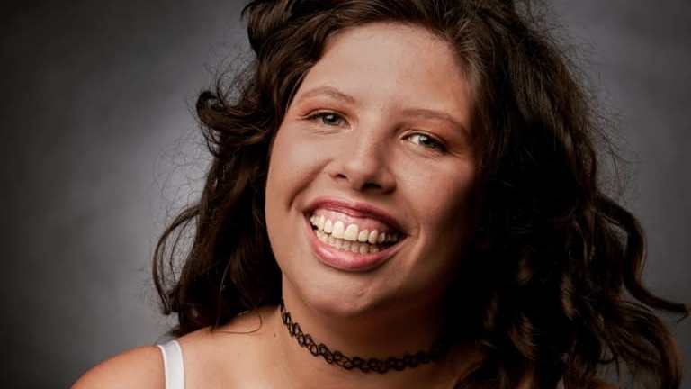 Jacinta Gregory smiling with curly hair and wearing a white tank top.