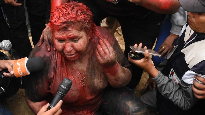 A woman sits on the ground covered in red paint.