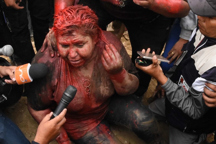 A woman sits on the ground covered in red paint.
