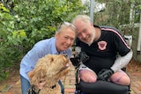 Man with bionic arms and no legs in a wheelchair, with his wife and a dog, smiling.