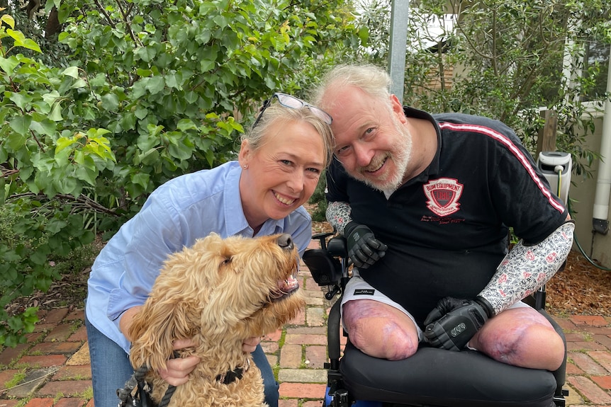 Man with bionic arms and no legs in a wheelchair, with his wife and a dog, smiling.
