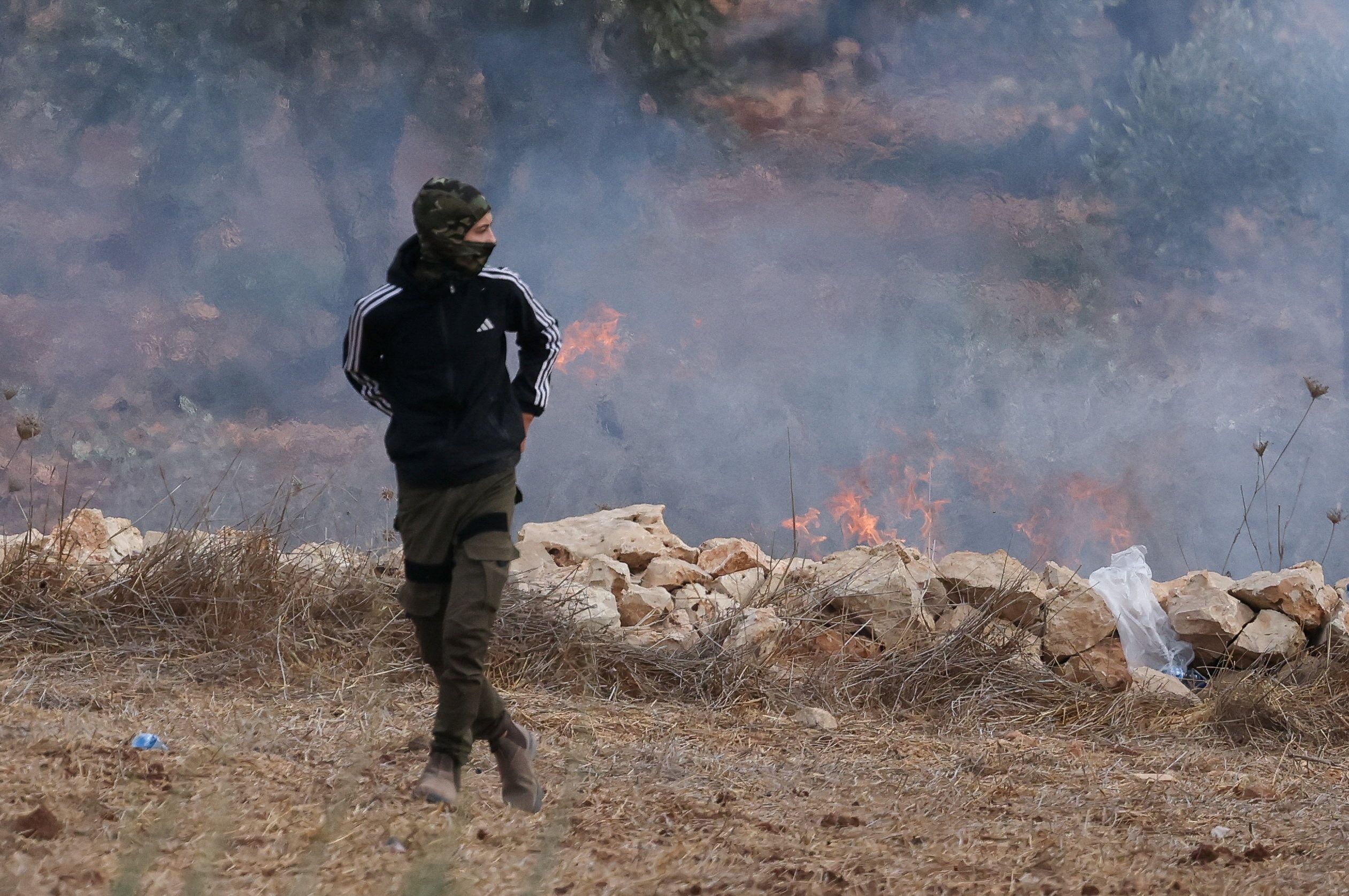 A young man runs away from a grass fire.