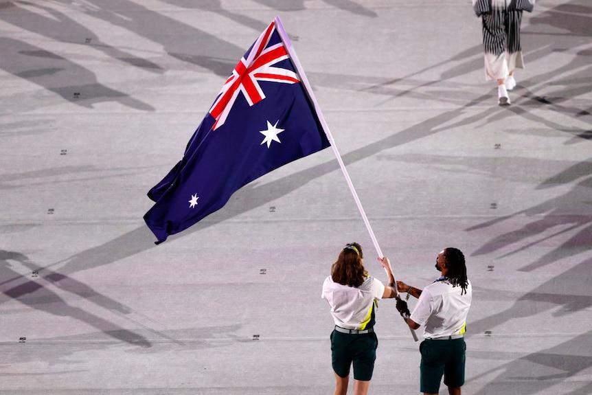 a high camera angle looking down on australia's olympic flagbearers. they are wearing green gold and white holding a large flag