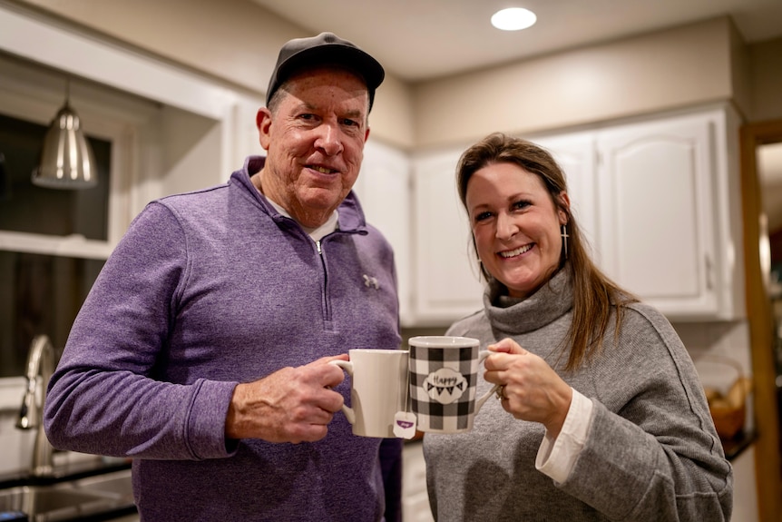 Scott and Vicki hold coffee cups in a kitchen. They are smiling for the camera.