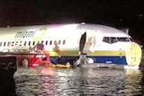 Rescuers approaching a plane, which appears to be floating in shallow water at night.