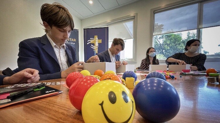 Two students and two researchers decorating small white boxes,  on a table strewn with decorations and stress balls.