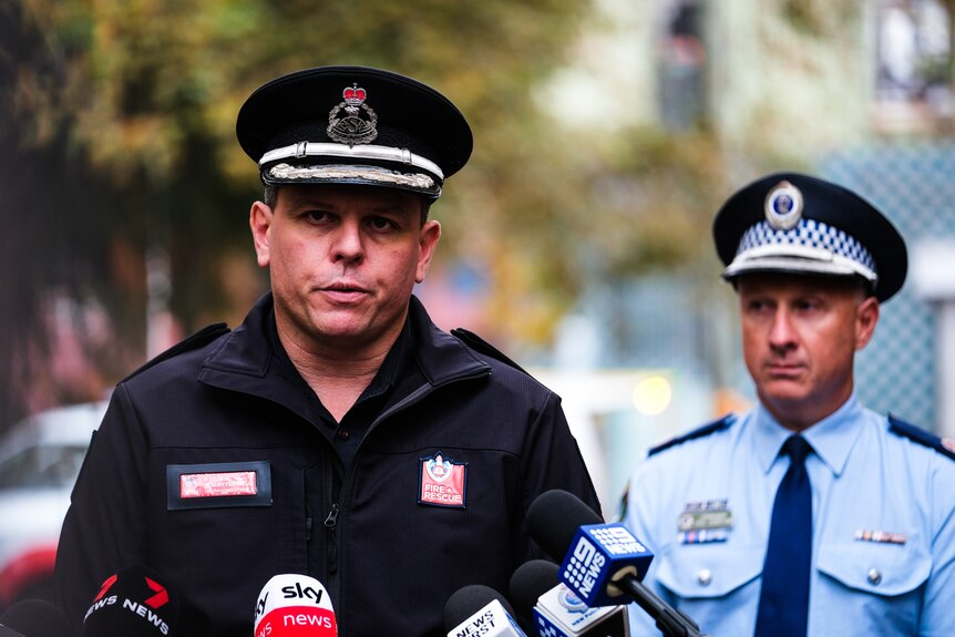 A man in a black fire brigade uniform stands next to a police officer