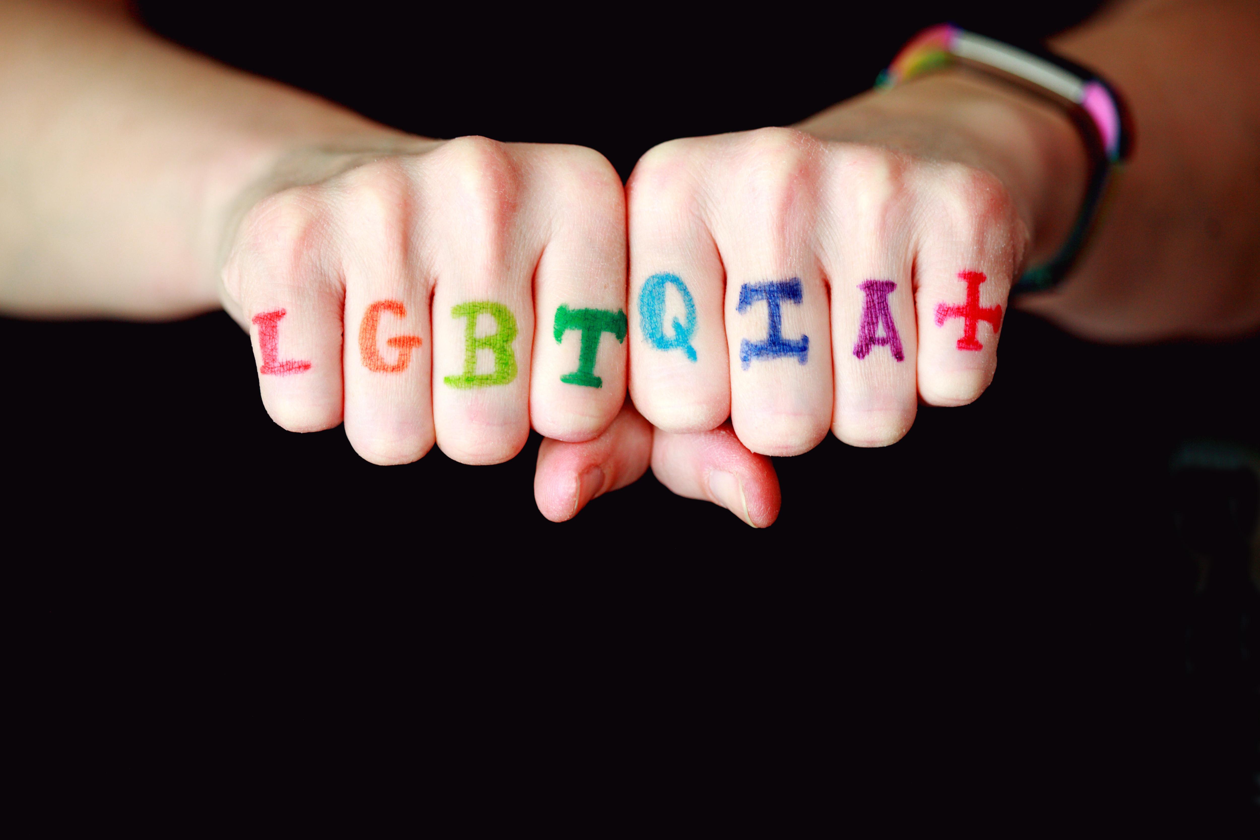 LGBTQIA+ written in rainbow colours on two fists