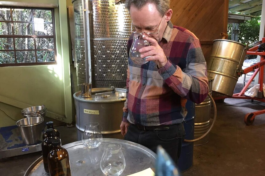 Man holds glass to smell the gin, inside a gin distillery