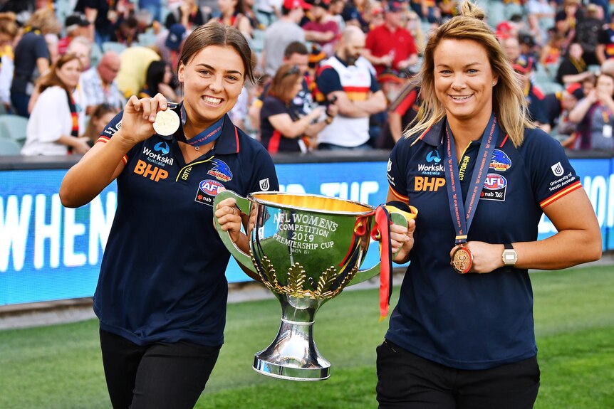 Ebony Marinoff and Courtney Cramey hold a large trophy while doing a lap of honour of Adelaide Oval.
