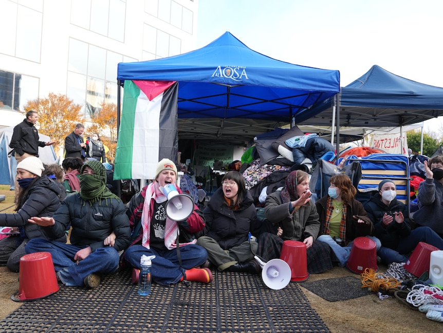 Protesters sit down and chant at the Australian National University pro-Palestine encampment.