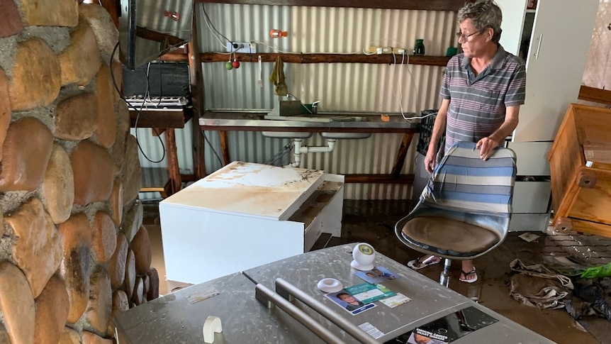 Clive Nesbitt looks at his belongings displaced and covered in mud, fridge on its side, cabinet and other furniture ruined.