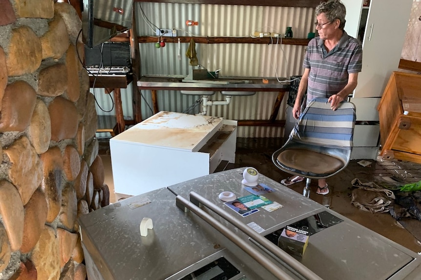 Clive Nesbitt looks at his belongings displaced and covered in mud, fridge on its side, cabinet and other furniture ruined.