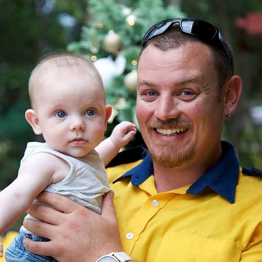 A smiling Geoffrey Keaton holds his son Harvey, while in his RFS uniform.