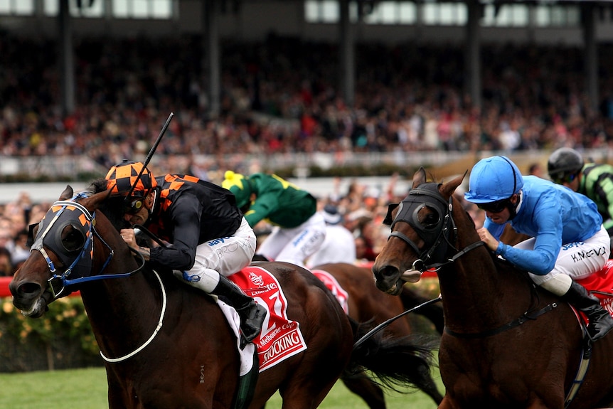 A jockey rides the leader in the Melbourne Cup with hands and heels as another horse chases behind him.