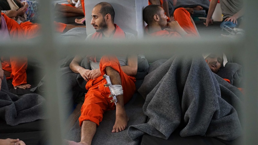 A prisoner with a leg brace is seen through the bars of a prison.