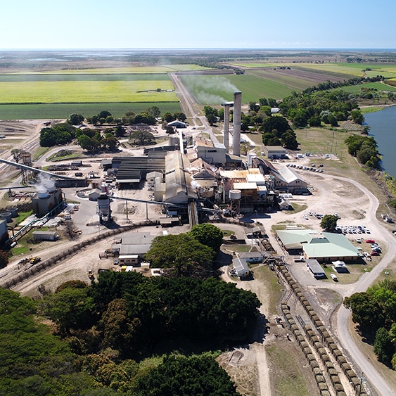 An aerial view of a sugar mill, with a river on the right and green fields in the background.