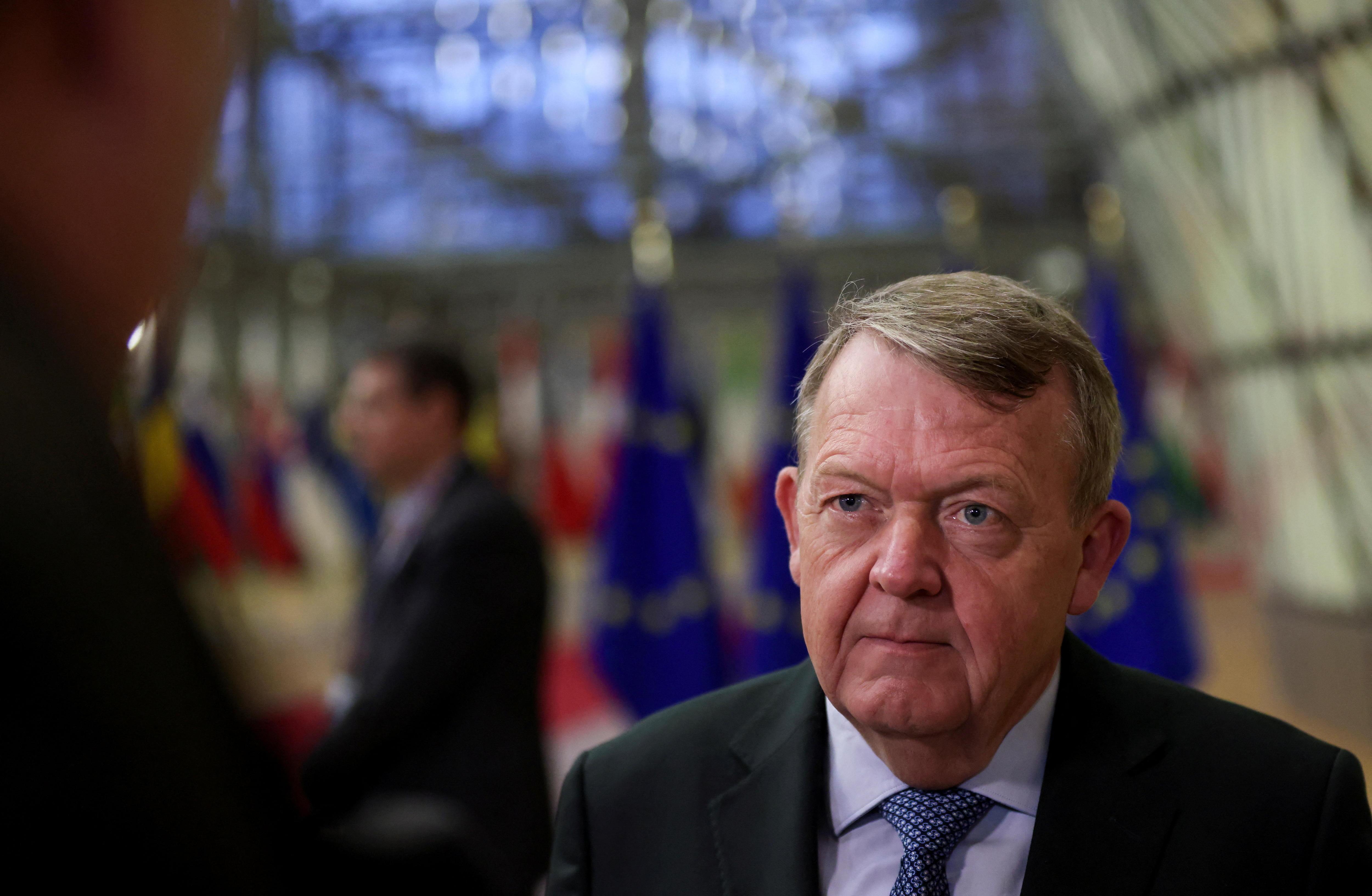 A middle-aged white man in a suit stands in front of row of EU flags at a conference.