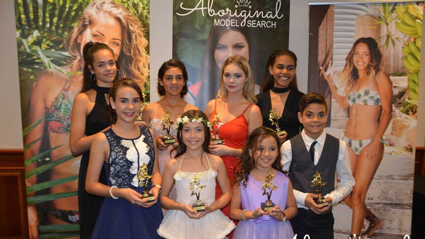 Eight Aboriginal models stand holding trophies.