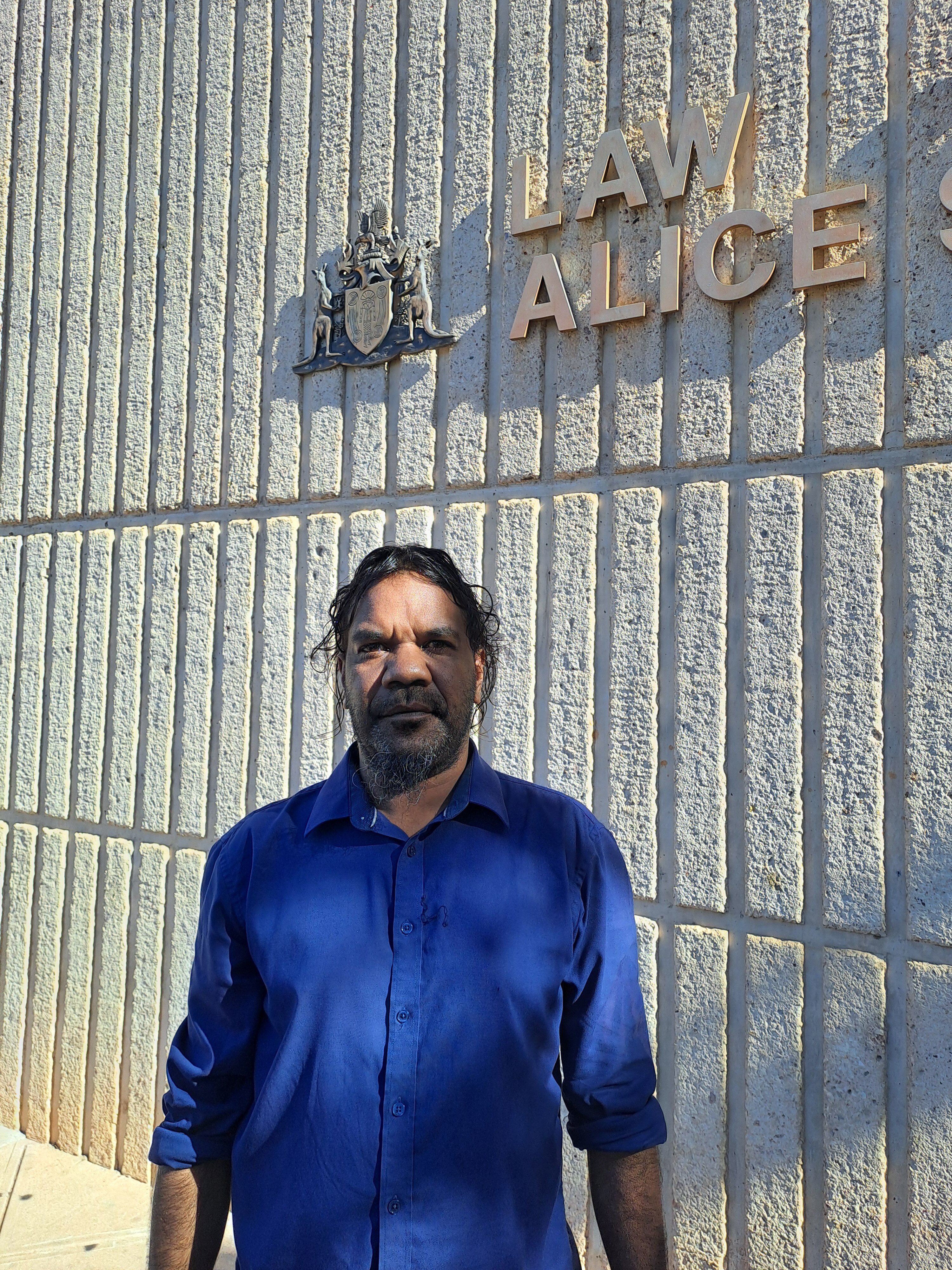 A man standing outside the wall of a building featuring a sign saying "Law Courts Alice Springs".