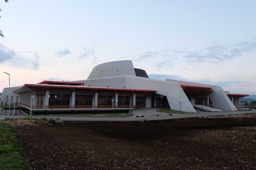 A new white tiled building with unusual angles is surrounded by dirt