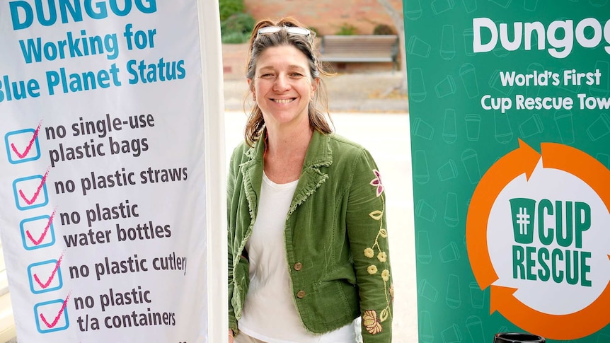 A woman in a green jacket stands between two large pull-up banners explaining the single use plastic free initiative