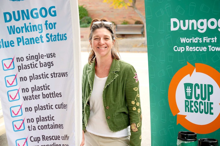 A woman in a green jacket stands between two large pull-up banners explaining the single use plastic free initiative