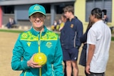 Ellen Ryan wears her Australian green and gold uniform while holding a yellow bowl on a bowling green, smiling.