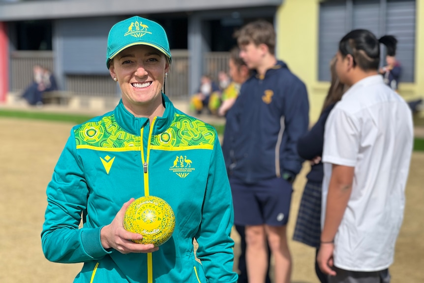 Ellen Ryan wears her Australian green and gold uniform while holding a yellow bowl on a bowling green, smiling.