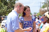 William and Kate smile as they speak to a group of bystanders. One holds a phone to record the meeting